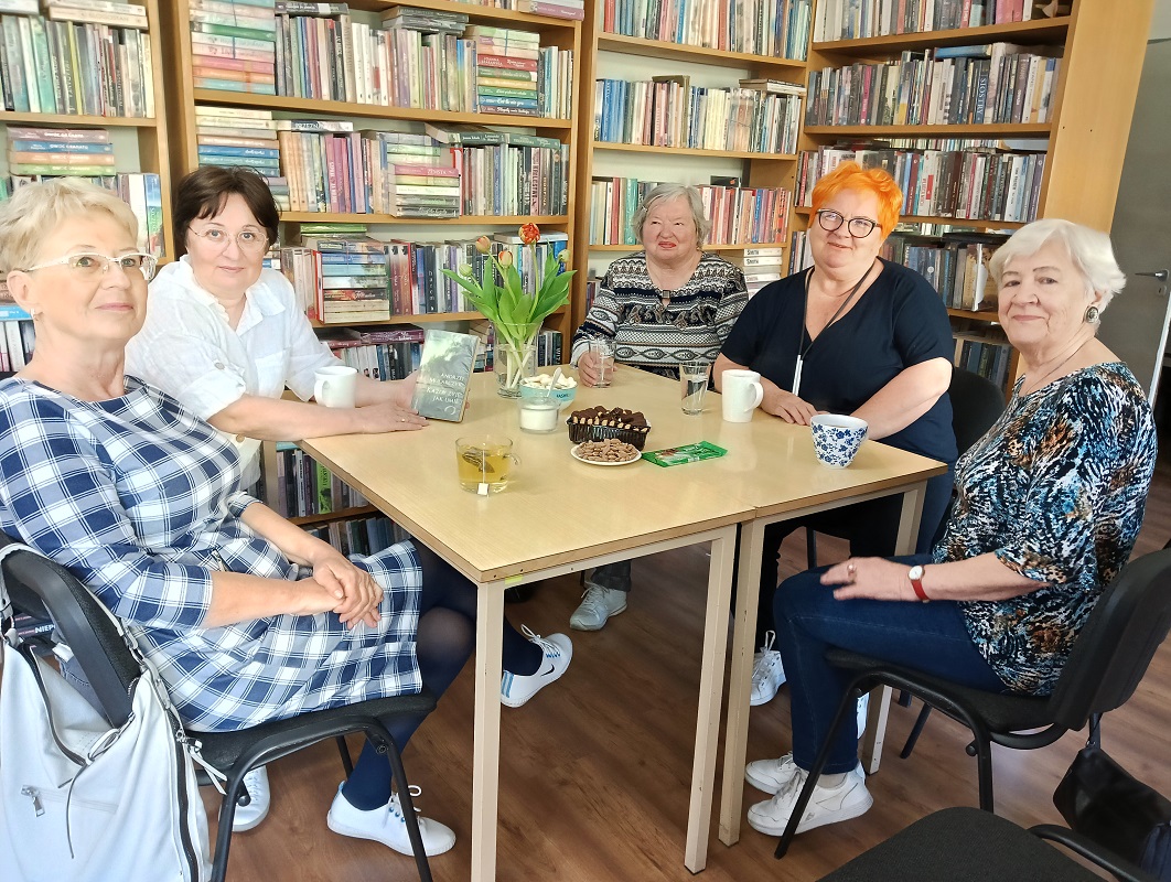 Na tle książek siedzące kobiety przy stoliku podczas spotkania "Maglownicy"