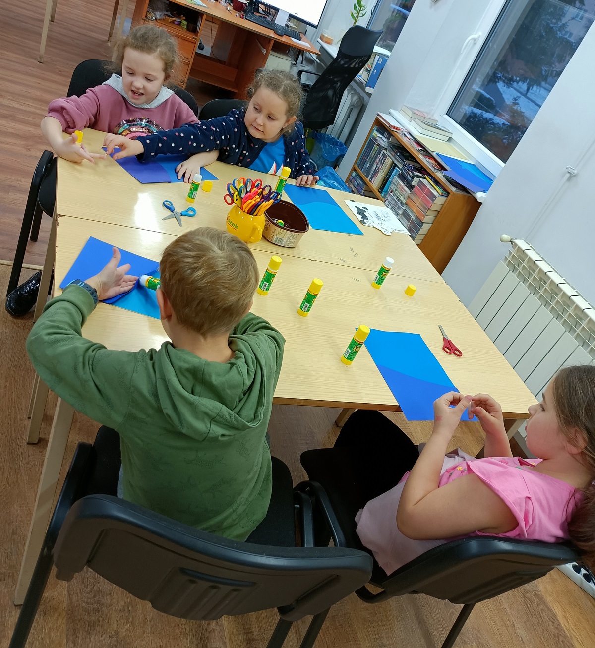 Dzieci z&nbsp;"Bajkownicy" podczas zajęć. Na niebieskiej kartce wyklejają niedźwiedzia.