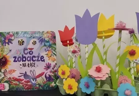 Zdjęcie przedstawiające okładkę książki pod tytułem Co zobaczę na łące? oraz pracę plastyczną w postaci kwiatowej łąki z papieru osadzonej w opakowaniu po jajkach