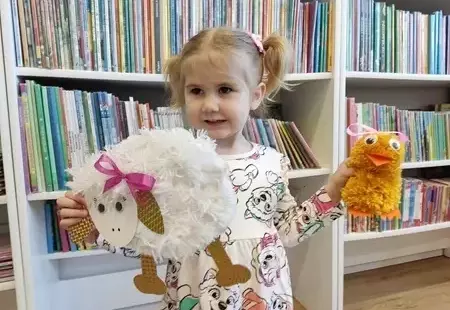 Zdjęcie przedstawiajace uśmiechniętą dziewczynkę trzymającą w ręku wykonane przez siebie prace plastyczne w postaci białego baranka i żółtej kury z wełny
