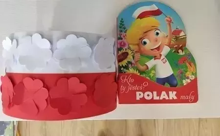 Zdjęcie przedstawia książkę pt "Kto ty jesteś Polak mały" oraz pracę plastyczną - patriotyczną opaskę z biało-czerwonymi kwiatami 