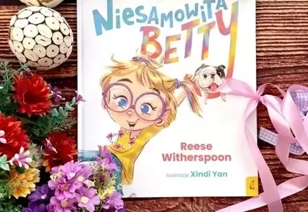 Okładka książki pod tytułem Niesamowita Betty na drewnianym stole a wokół niej kolorowe kwiaty
